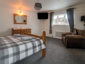 A bedroom with a wooden bed with checked bedding a wooden dresser with a mirror a wall-mounted tv a brown sofa and grey curtains at Bobbys Lodge in South Chard