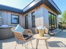 An outdoor patio with two wicker chairs a round table with a champagne bucket and a wooden house exterior at Little Victory in Pendeen