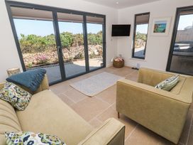A sitting room with two beige sofas a small rug a wall mounted tv and large windows overlooking a garden at Little Victory in Pendeen