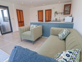 A living area with green sofa and armchair with patterned cushions near a kitchen counter with wooden doors at Little Victory in Pendeen