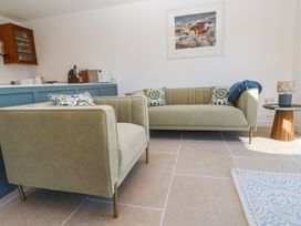 A living room with two sofas a side table with a lamp and a kitchen counter with appliances at Little Victory in Pendeen