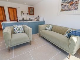 A living area with a green armchair and sofa with patterned cushions near a blue kitchen counter at Little Victory in Pendeen