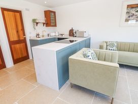 A kitchen area with blue cabinets a white countertop a wooden door beige tiled floor and green upholstered armchairs at Little Victory in Pendeen