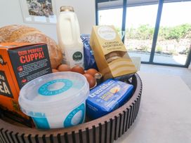 A basket with bread eggs milk butter biscuits tea and sea salt in a room with sliding glass doors at Little Victory in Pendeen
