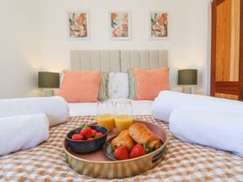 A bed with orange and striped pillows bedside lamps and a tray with croissants strawberries and orange juice at Little Victory in Pendeen