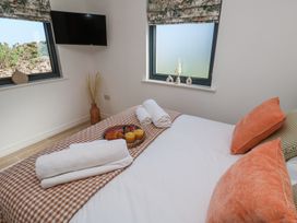A bedroom with a bed with orange pillows towels and breakfast tray near windows and a wall mounted tv at Little Victory in Pendeen
