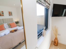 A bedroom with a bed with orange pillows and a checkered bedspread seen in a mirror next to a window with a vase on the sill and a wall-mounted TV at Little Victory in Pendeen