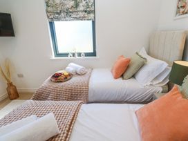 A bedroom with two single beds with orange and green pillows and a window with floral blinds at Little Victory in Pendeen