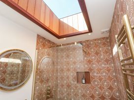 A bathroom with patterned tiles a glass shower enclosure a round mirror and a skylight window at Little Victory in Pendeen