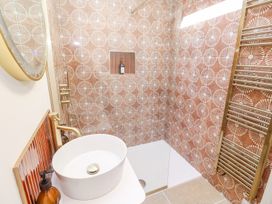 A bathroom with a vessel sink a round mirror a shower area with patterned tiles and a heated towel rail at Little Victory in Pendeen