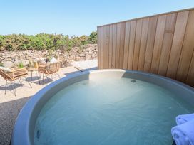 An outdoor hot tub with water and towels next to a patio with two wicker chairs and a small table at Little Victory in Pendeen