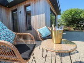 An outdoor patio with two wicker chairs with cushions and a table with a gold ice bucket and glasses at Little Victory in Pendeen