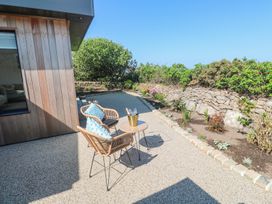 An outdoor patio area with two wicker chairs and a small round table with a bucket on it next to a garden bed with plants and flowers at Little Victory in Pendeen