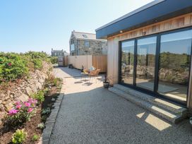 An outdoor patio area with two chairs a small table flower beds and large glass sliding doors at Little Victory in Pendeen