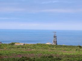 A coastal view with a metal structure and buildings behind green shrubbery and flowers at Little Victory in Pendeen