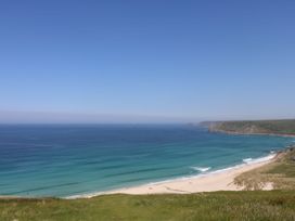 A sandy beach with waves and a rocky coastline under a clear blue sky at Little Victory in Pendeen