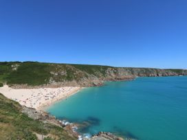 A beach with people on sand next to turquoise sea and rocky cliffs under clear blue sky at Little Victory in Pendeen