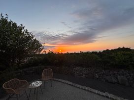 An outdoor patio area with two wicker chairs and a small table at sunset surrounded by bushes and a stone wall at Little Victory in Pendeen