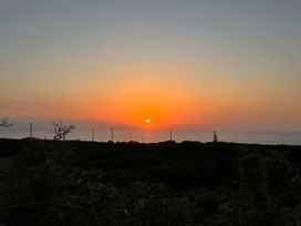 A sunset over the sea with silhouette of bushes and utility poles at Little Victory in Pendeen