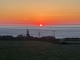 A sunset over the ocean with buildings and power lines in the foreground at Little Victory in Pendeen