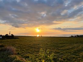A sunset over a grassy field with scattered houses and power lines near the coast at Little Victory in Pendeen