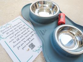 A pet feeding station with two stainless steel bowls a roll of red dog waste bags and a welcome note for dogs at Little Victory in Pendeen
