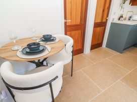 A small dining area with a round wooden table set for two and white cushioned chairs near wooden doors and a kitchen counter at Little Victory in Pendeen