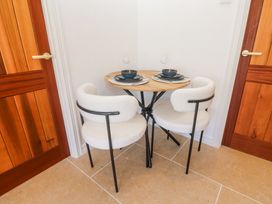 A small round wooden table with two white cushioned chairs and table settings between two wooden doors at Little Victory in Pendeen