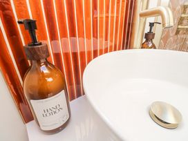 A bathroom sink with a gold faucet and a brown bottle of hand lotion next to orange tiled wall at Little Victory in Pendeen