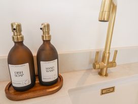 A kitchen sink area with two bottles labeled dish soap and hand wash beside a brass faucet at Little Victory in Pendeen