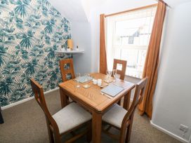 A dining room with a wooden table and four chairs near a window with orange curtains and a wall with green leaf patterned wallpaper at Medical Hall in Cemaes Bay