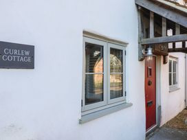 The exterior of a white cottage with a red door a window and a sign that says Curlew Cottage at Curlew Cottage in North Curry near Taunton