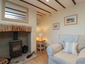 A sitting room with a wood burning stove a small wooden side table lamp and an armchair with cushions at Curlew Cottage in North Curry near Taunton