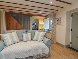 A sitting area with a light blue sofa with striped cushions near wooden staircase and shuttered window at Curlew Cottage in North Curry near Taunton