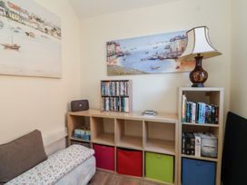 A corner of a room with a wooden shelving unit containing books dvds and storage bins and a lamp on top at Curlew Cottage in North Curry near Taunton