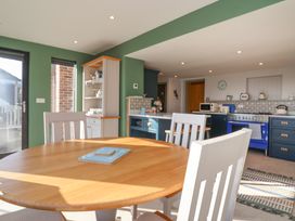 A kitchen with a round wooden table and white chairs a blue oven and green walls at Curlew Cottage in North Curry near Taunton