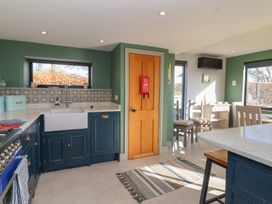 A kitchen with blue cabinets green walls a white sink a wooden door and dining table at Curlew Cottage North Curry near Taunton