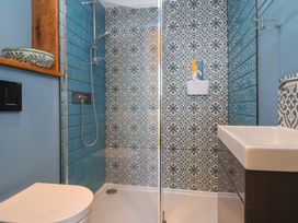 A bathroom with a walk-in shower featuring blue and patterned tiles a toilet a sink and a wall-mounted ceramic bowl at Curlew Cottage in North Curry near Taunton