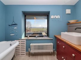 A bathroom with a clawfoot bathtub a radiator under a window a wooden cabinet with a sink and outdoor view at Curlew Cottage in North Curry near Taunton