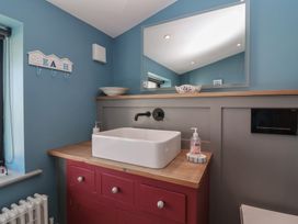 A bathroom with a white rectangular sink on a wooden countertop and red cabinets a large mirror and blue walls at Curlew Cottage in North Curry near Taunton