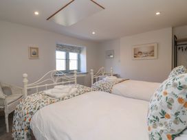 A bedroom with two single beds white bedding floral pillows a window and a wicker chair at Curlew Cottage in North Curry near Taunton