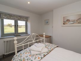 A bedroom with a metal bed frame white towels on the bed a window with a floral valance and a small dresser on the side at Curlew Cottage in North Curry near Taunton