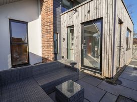 An outdoor patio area with gray woven sectional sofa and a small glass-top table next to a wooden and brick exterior wall at Curlew Cottage in North Curry near Taunton