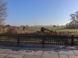 A paved patio area with a wooden lattice fence overlooking a field with trees and shrubs at Curlew Cottage in North Curry near Taunton