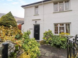 Front entrance of a white house with black door and garden with plants and stone path at Maiden Moor in Grange near Keswick