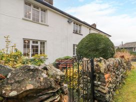A stone wall with a metal gate and bushes in front of a white house at Maiden Moor in Grange near Keswick