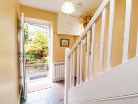 A hallway with a white wooden staircase an open door showing a garden outside at Maiden Moor in Grange near Keswick