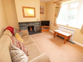 A living room with a beige sofa with cushions a fireplace a television on a wooden stand and a wooden coffee table by a window at Maiden Moor in Grange near Keswick