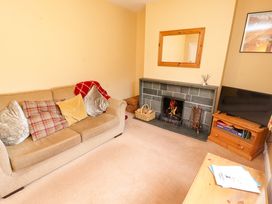 A living room with a beige sofa and cushions a fireplace with a fire a wooden mirror a television on a wooden cabinet and a wooden table with papers at Maiden Moor in Grange near Keswick