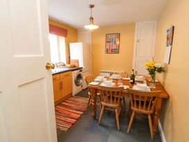 A kitchen with a wooden dining table set for six a refrigerator washing machine and a colorful rug Maiden Moor Grange near Keswick